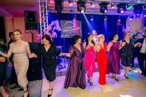Group of dancers in elegant dresses perform under purple stage lighting at formal event.