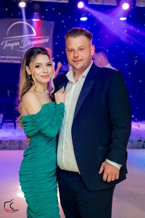 Formal event couple poses against blue-lit backdrop with professional lighting and event logo.