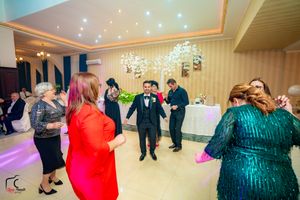 People dancing together in a brightly lit ballroom with chandeliers and colorful lighting.