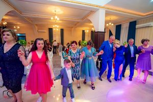 Party guests in colorful dresses performing a group dance in an elegant ballroom.
