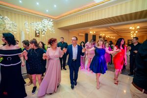 Formal event guests dancing in a line under elegant chandeliers.