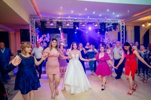 Wedding reception dance party with guests in colorful dresses under purple lighting.
