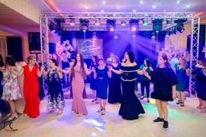 Wedding guests dance together in a ballroom illuminated by purple and pink lighting during a reception celebration.