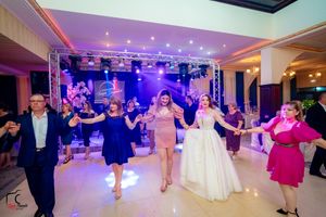 Wedding reception guests form a dance line while celebrating under colorful event lighting.
