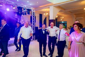 Wedding attendees join hands in a circle dance during an evening reception with purple ambient lighting.