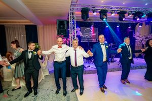 Wedding celebration features guests performing traditional line dances on an illuminated dance floor.