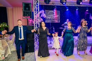Party guests dancing in a line on a dance floor with blue and purple lighting and stage equipment.