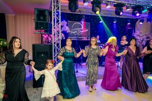 Wedding party members dance in elegant formal attire under vibrant purple and blue lighting.