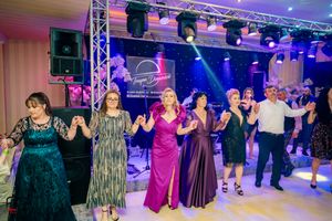 Group dancing in formal attire under blue and purple stage lights at an indoor event.