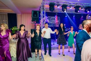 People dancing in a line wearing formal dresses under blue stage lighting at a celebration.