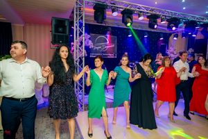People in formal wear dancing in a line at an indoor celebration with professional lighting.