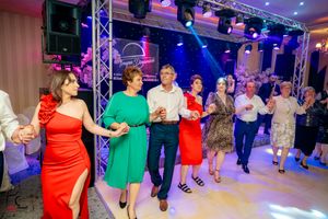 Guests in vibrant dresses performing coordinated dance moves at an indoor celebration.