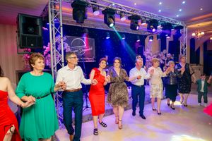 Celebration attendees in formal wear dancing in a line under professional stage lighting.