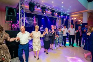 Large group of party guests dancing in a line formation at an indoor venue with atmospheric lighting.