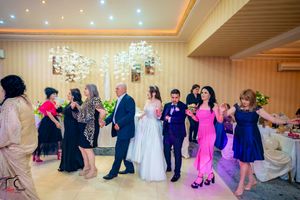 Wedding reception guests dancing in a line on a ballroom floor under colorful lighting and decorations.