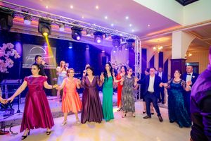 Panoramic view of wedding reception dance floor with guests in formal attire under purple lighting.
