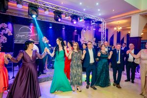 Wedding celebration showing guests in formal wear dancing in formation across illuminated ballroom.