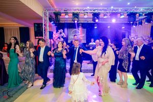 Wedding reception dance floor panorama showing guests in colorful attire under stage lighting.