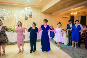 Wedding guests dance in a line formation wearing coordinated blue and pink outfits at an indoor reception venue.