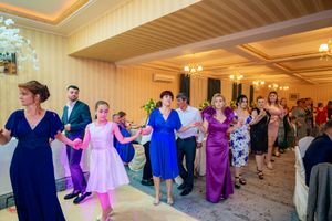 Large group performs synchronized dance moves in formal attire under chandeliers at an elegant venue.