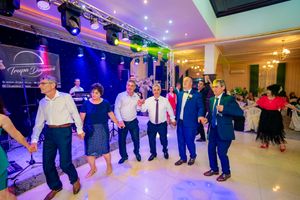 Wedding guests perform traditional line dance under colorful lighting at indoor reception.