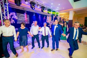 Large group participates in synchronized dance at wedding reception with purple and blue lighting effects.