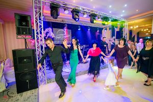 Wedding celebration features group dancing under vibrant stage lighting and professional sound equipment.