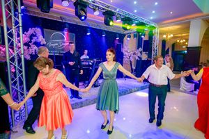 Large group dancing in formation at an elegant ballroom venue with colorful stage lighting.