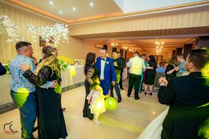 Wedding party dancing under decorative lighting in a spacious ballroom with striped wallpaper.