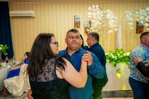Wedding guests dancing and socializing in a warmly lit reception venue with floral decorations.