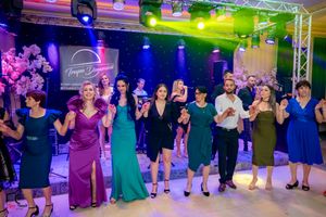 Wedding party participants lined up doing group dance moves under vibrant stage lighting.