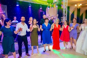 Celebration attendees performing choreographed dance routine in formal attire under multicolored lights.