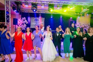 Wide shot of wedding reception dance floor with guests performing synchronized moves under theatrical lighting.
