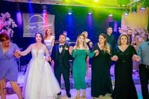 Wedding party and guests performing line dance under vibrant multicolored stage lighting.