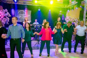 Partygoers dance in a line on a colorfully lit dance floor with blue and green stage lighting.