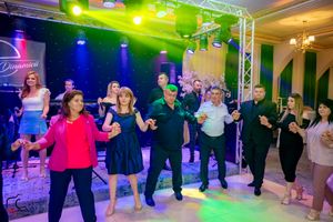 Party attendees perform a synchronized line dance under colorful stage lighting at an indoor venue.
