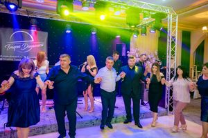Group of dancers holding hands in a line at an event with vibrant blue and green lighting effects.