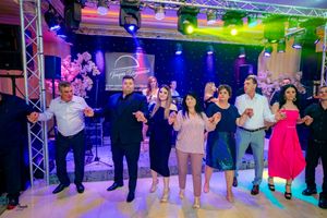 Group performs coordinated dance moves at an indoor event with professional lighting and sound equipment.