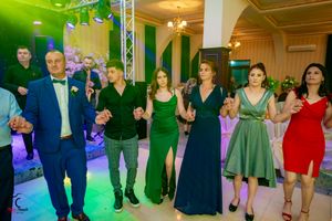 Formal event attendees in elegant attire dance together under dramatic green and purple lighting.