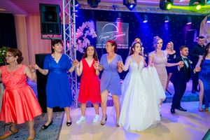 Wedding reception dance floor filled with guests in colorful dresses under blue and purple lighting.