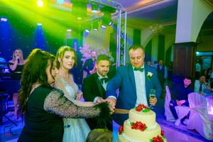 Wedding reception venue illuminated with vibrant green and blue lighting as guests gather around a tiered cake.
