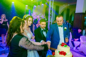 Wedding celebration with colorful mood lighting showing guests gathered near a white tiered cake.