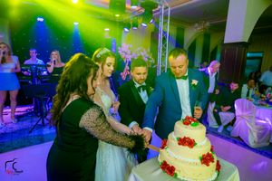 Elegant wedding reception space with theatrical lighting and guests surrounding a multi-tiered white cake.