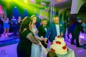 Wedding venue bathed in colorful lights while guests celebrate around an ornate white cake.