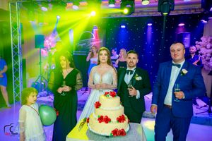 Wedding reception hall with theatrical lighting and guests gathered around a white tiered cake.