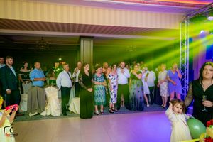 Wedding reception guests gather on a dance floor illuminated by colorful green and purple lighting effects.
