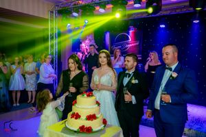 A wedding celebration with a tiered cake adorned with red roses under dramatic stage lighting.