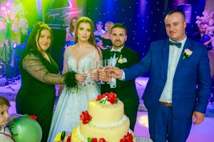 Wedding celebration with guests toasting around an elegant tiered cake decorated with red roses.