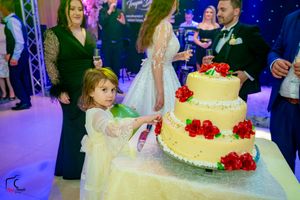 Young attendee admires the elegant wedding cake decorated with red roses during reception.