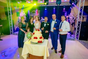 Wedding party gathered around an elegant tiered cake under dramatic blue and green lighting.